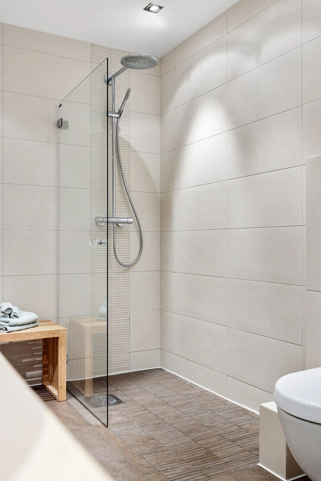 Elegant modern bathroom featuring a glass shower and minimalist design with neutral tiles and wooden accents