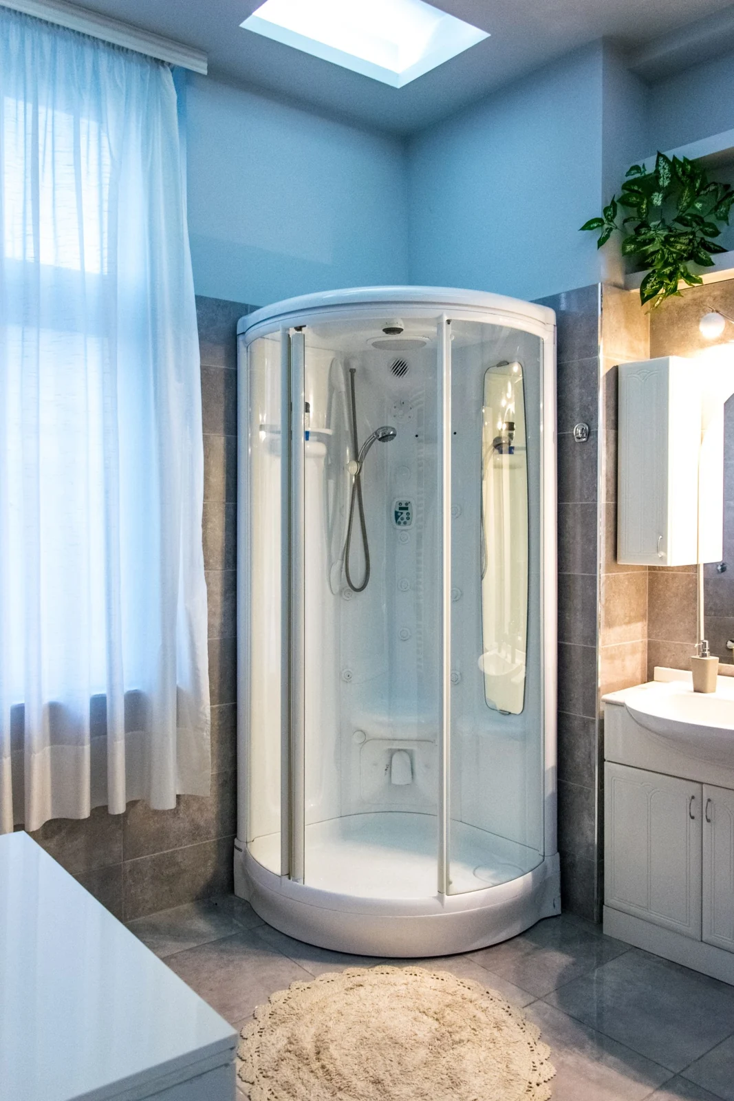 Bright and elegant home bathroom interior with a curved glass shower, natural light, and minimal decor