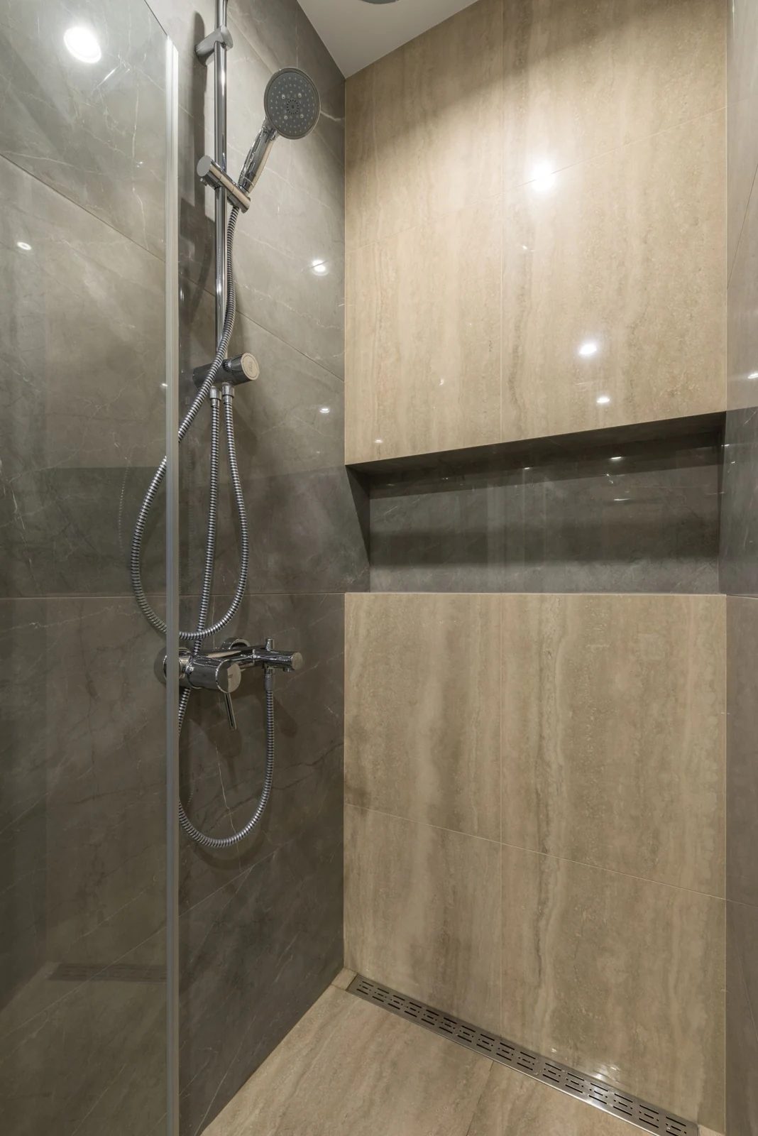 Shower cabin with chrome faucets and shiny tiled walls in modern illuminated bathroom